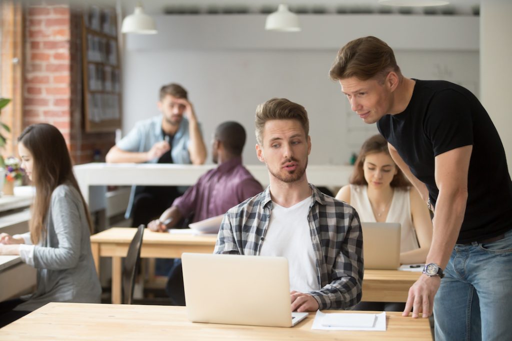 busy-office-man-looking-over-colleague's-shoulder-micro-managing